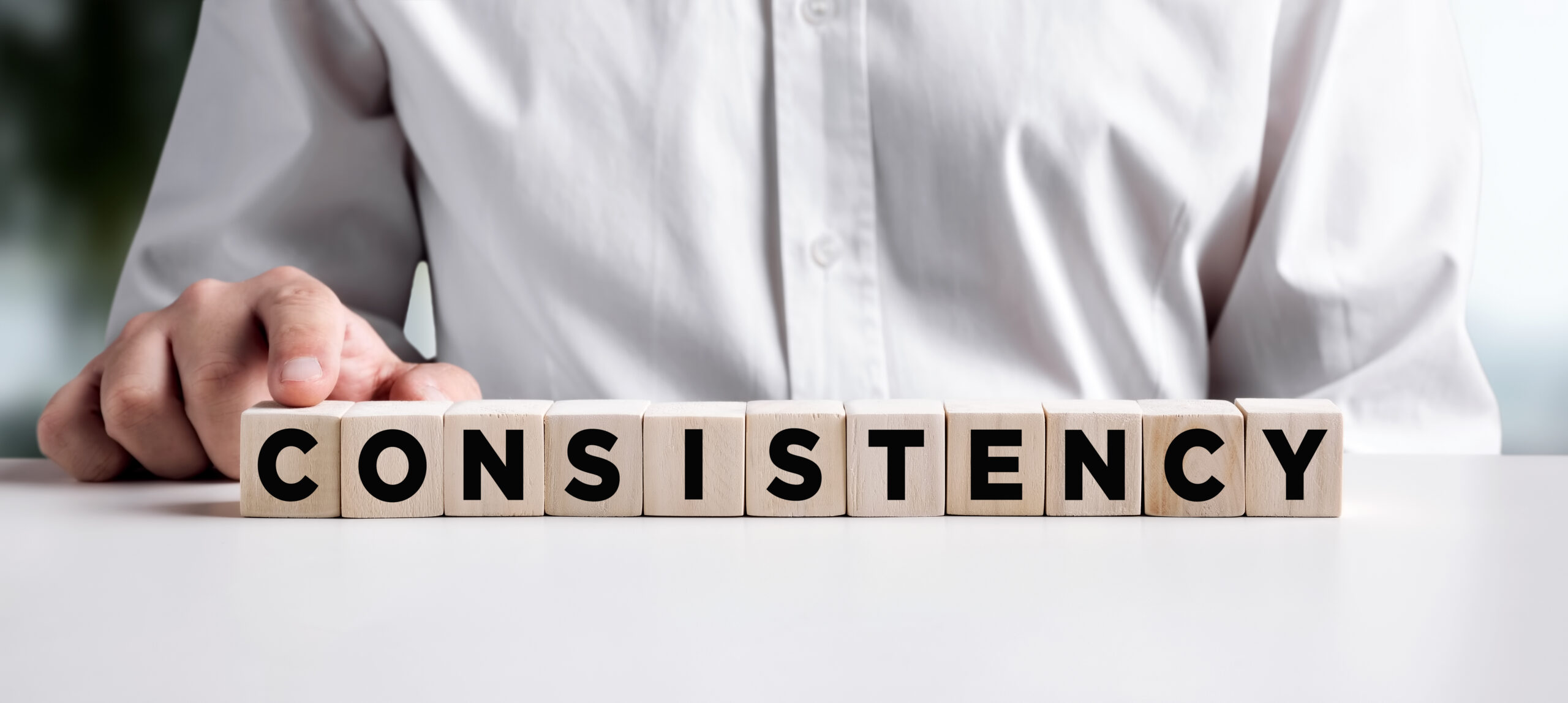 Well-dressed person aligning wooden blocks to spell out consistency