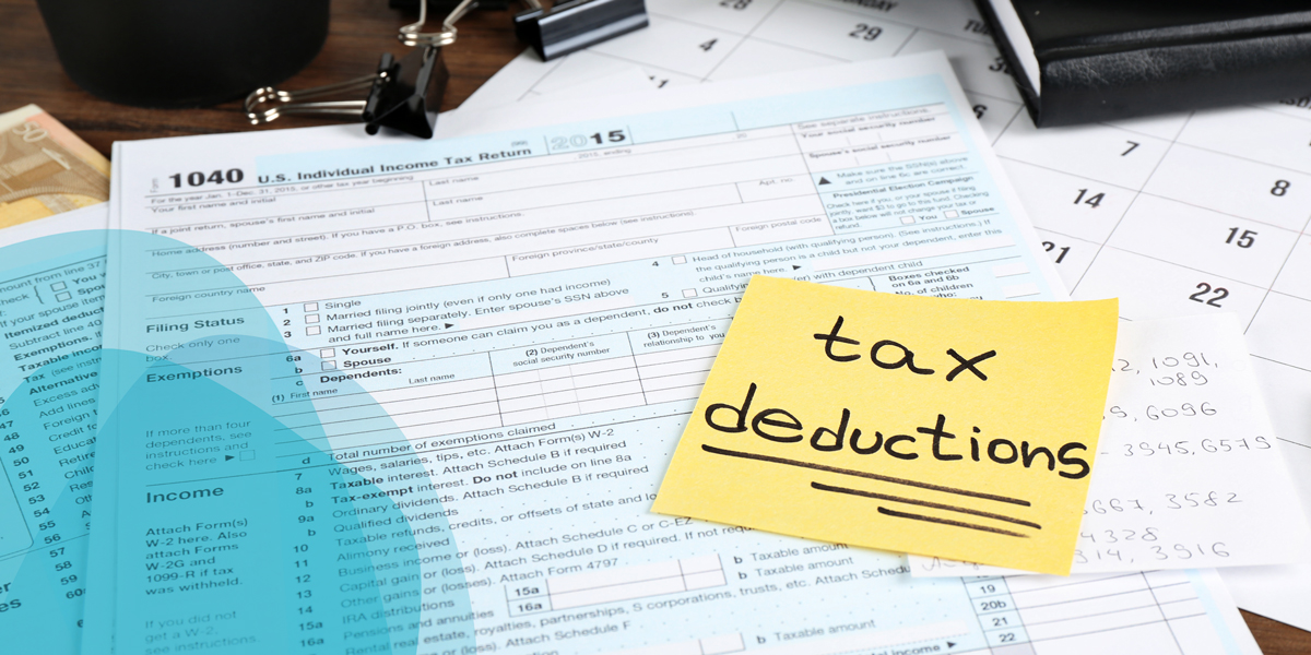 Forms for filing taxes spread out on a desk with a yellow stick note that reads "tax deductions"